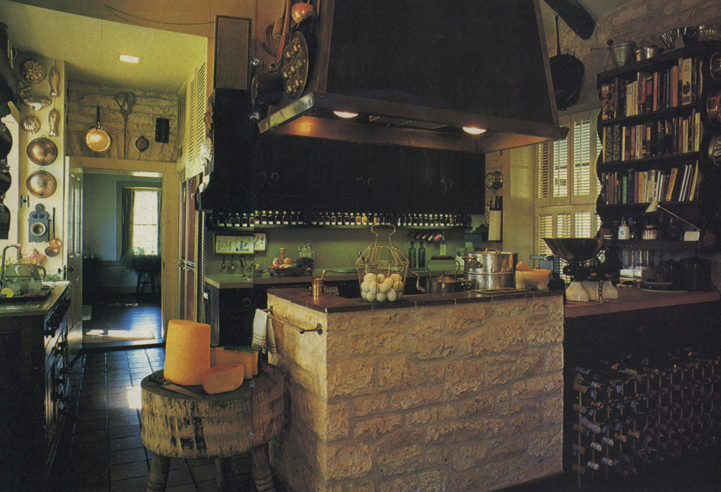 Most living and entertaining take place in the combination kitchen and informal living room (behind camera, not shown), a prime example of what Bell means by treating a house with "sympathy if not honesty": The beams in the ceiling were originally in the floor, the iron stove under the copper-accented hood came from a girl's school, and the stone in the room divider was salvaged from an old smokehouse that once stood on the property.