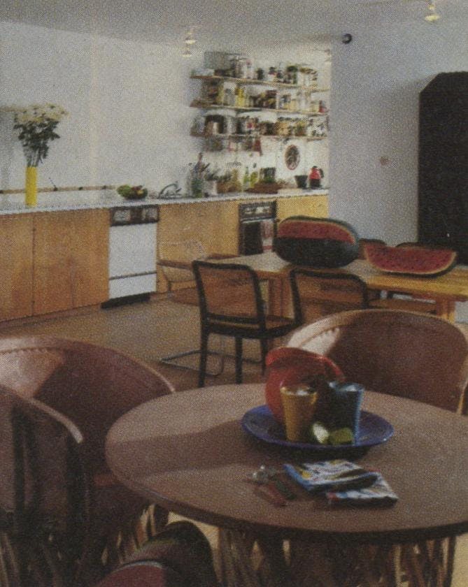 The open shelves over the kitchen counter hold an array of foods ranging from pasta to imported chutneys. In the foreground are a Mexican table and chairs of cowhide and split cedar. 