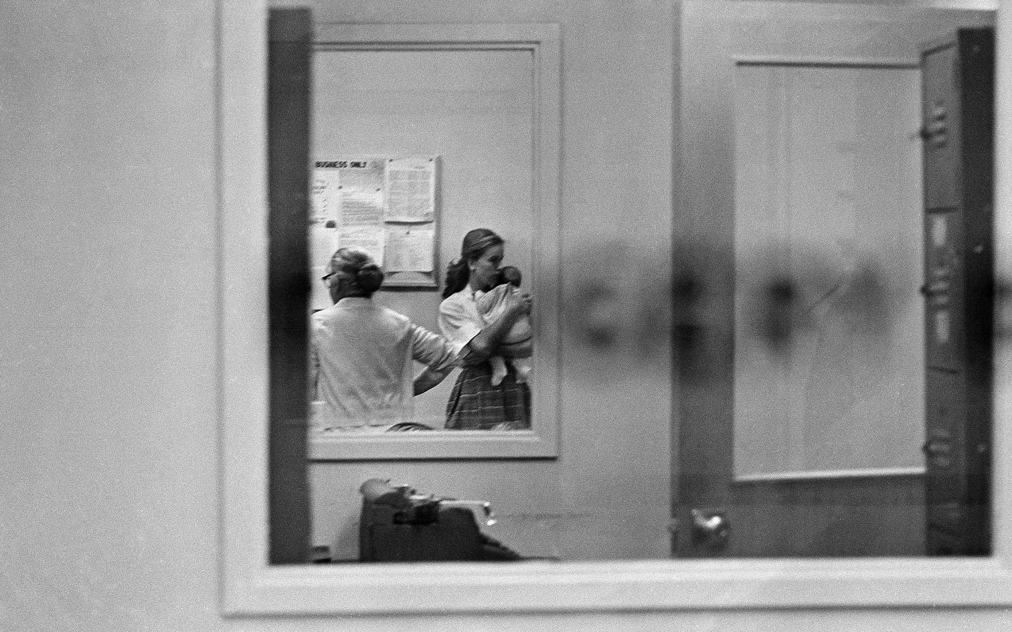 Marina, holding a baby Rachel, and Marguerite Oswald seen through a window in the Dallas police station.