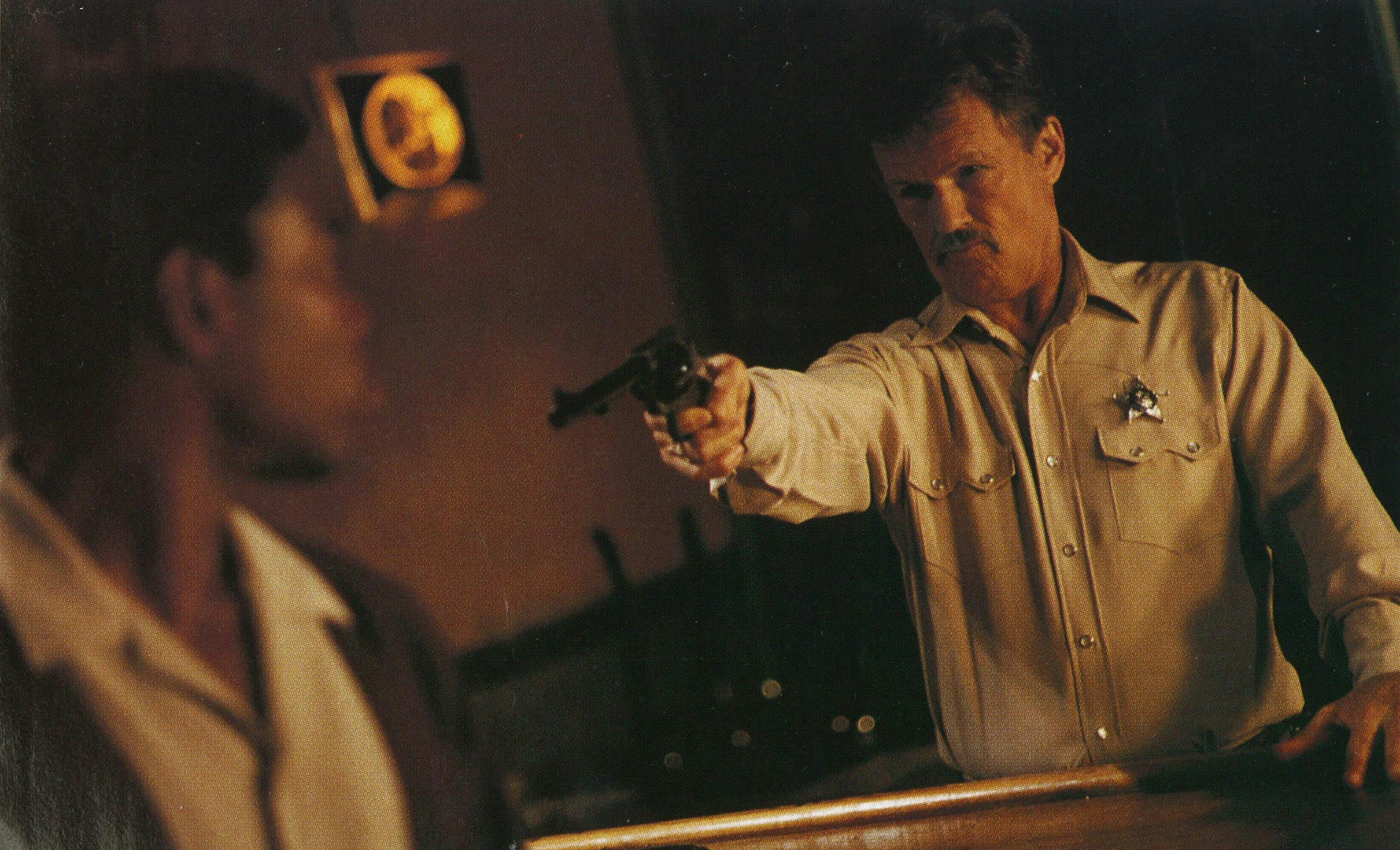 Still from Lone Star of Kristofferson pointing a gun at someone out of focus.