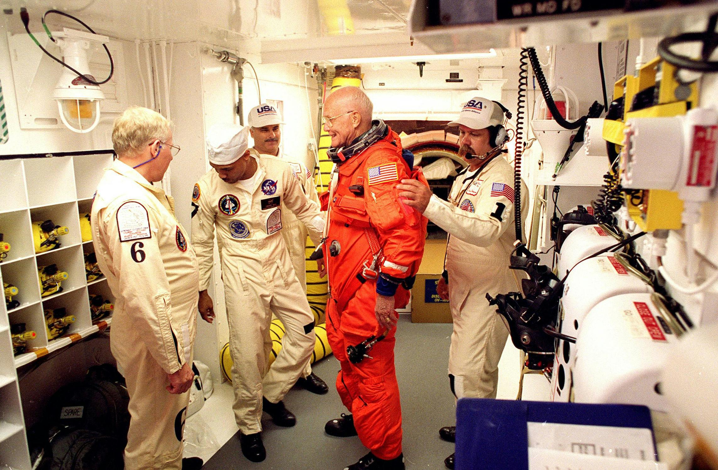John Glenn getting dressed in an orange spacesuit. 