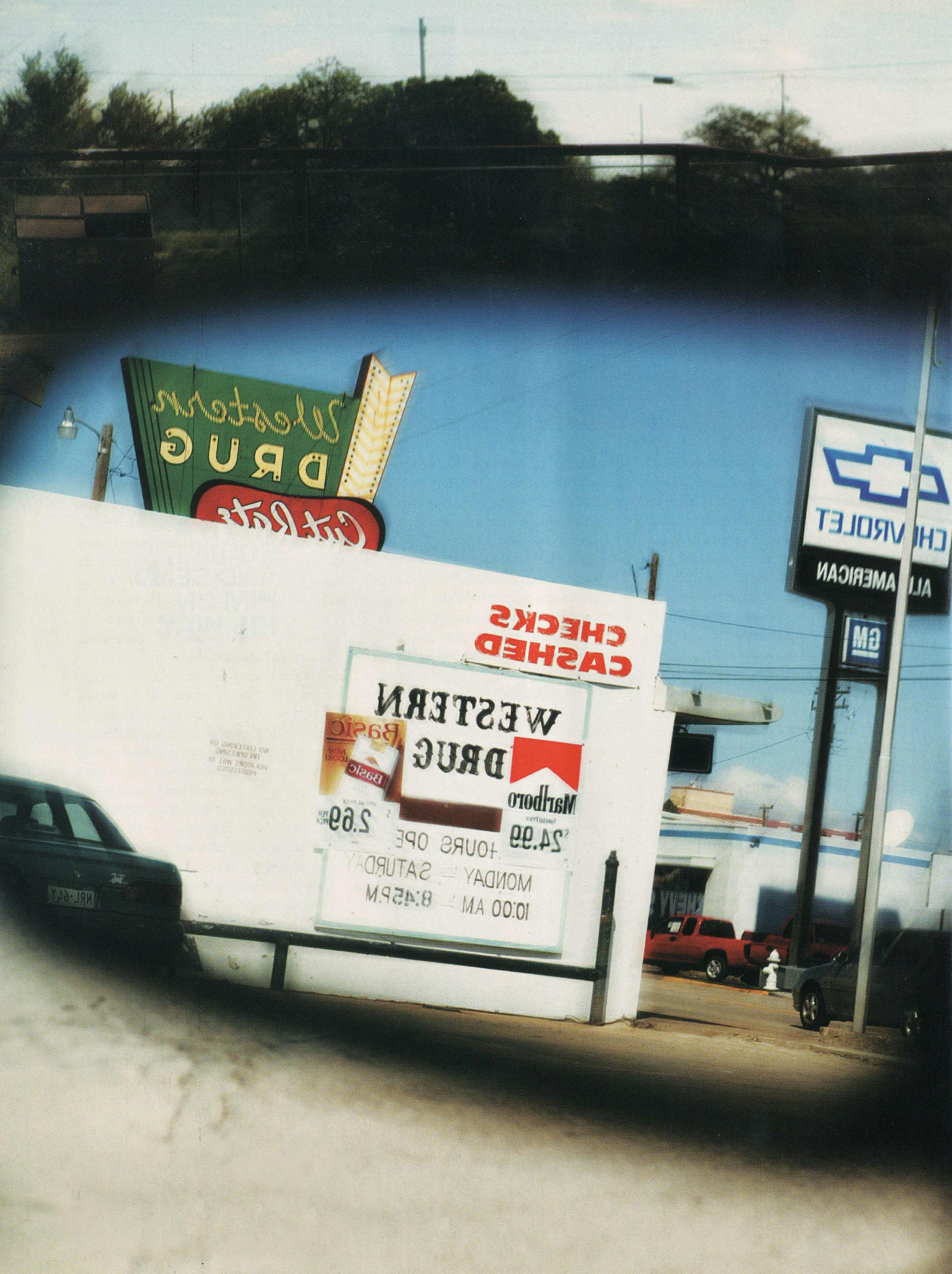 Signs for a drugstore and a car dealership in a rear-view mirror. 