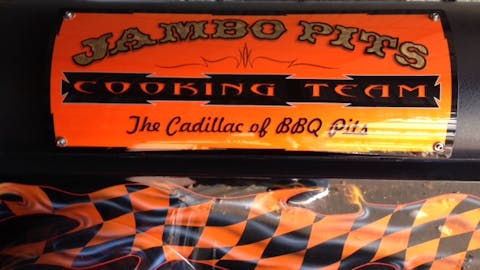 A custom painted pit reading, "Jambo Pits cooking team: the cadillac of BBQ Pits."