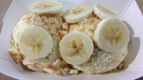 Two round scoops of banana pudding topped with fresh, sliced bananas. 