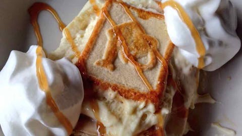 Scoop of banana pudding with two dollops of whipped cream and a drizzle of caramel syrup. 
