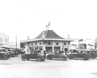 Black and white photo of old cars in front of the pig stand. 