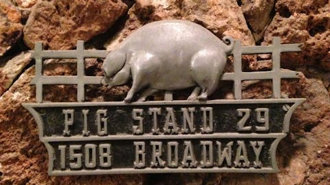 A metal sign with a pig in front of a fence. 