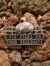 A metal sign with a pig in front of a fence. 