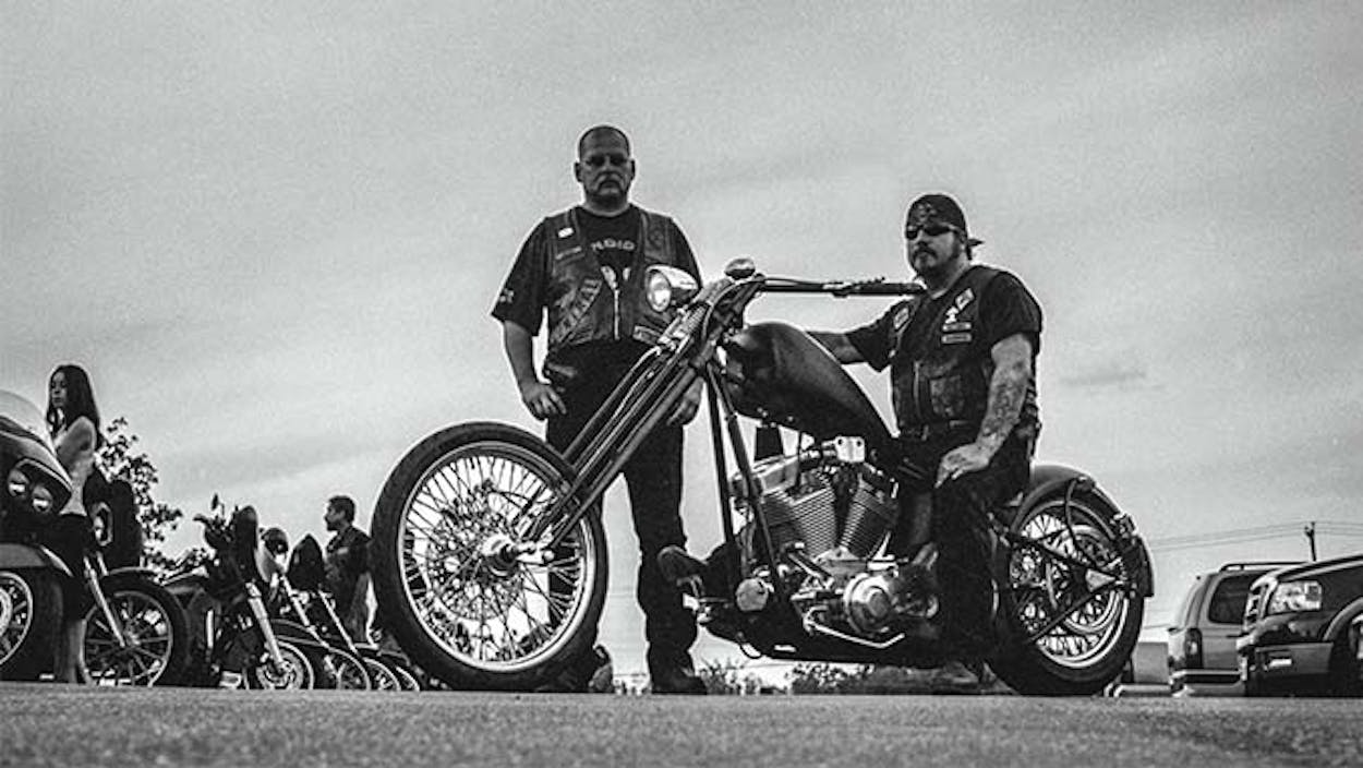 Black and white photo of one Bandidos member on his motorcycle and another standing beside him.