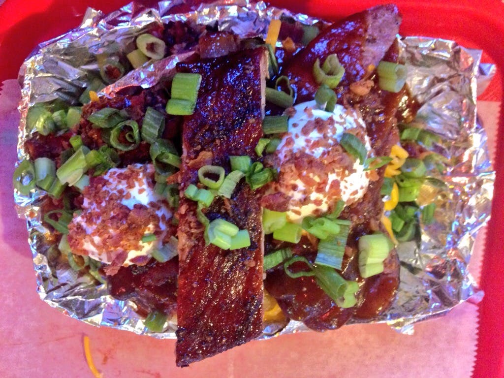 Baked potato topped with sour cream, bacon bits, chives, and a large pork rib. 