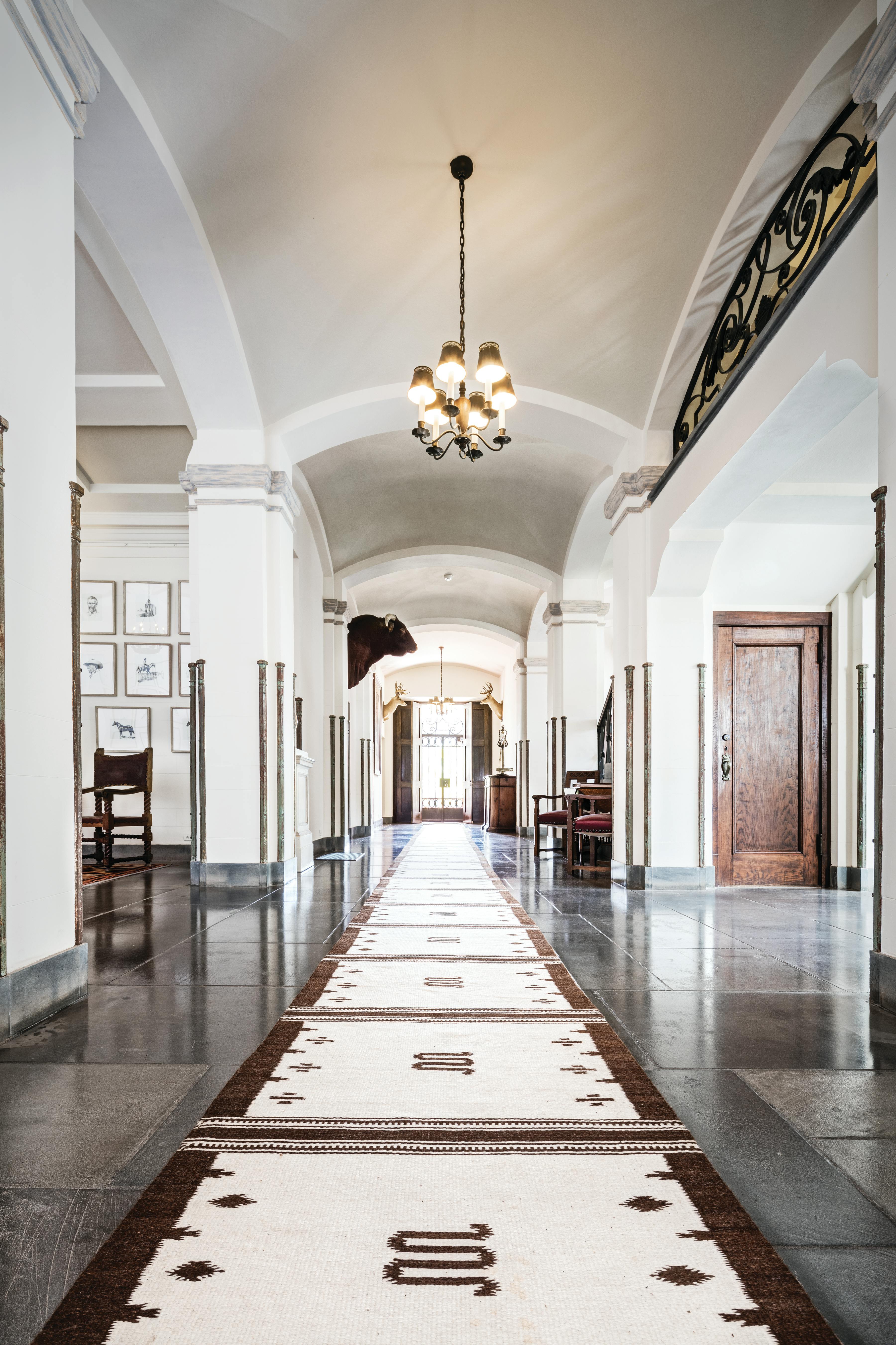 The front hall on the first floor features archways, columns, marble floors, and Tiffany-designed chandeliers. The sixty-foot runner on the floor was made in a saddle blanket design by King Ranch master weaver Emiliano Garcia.