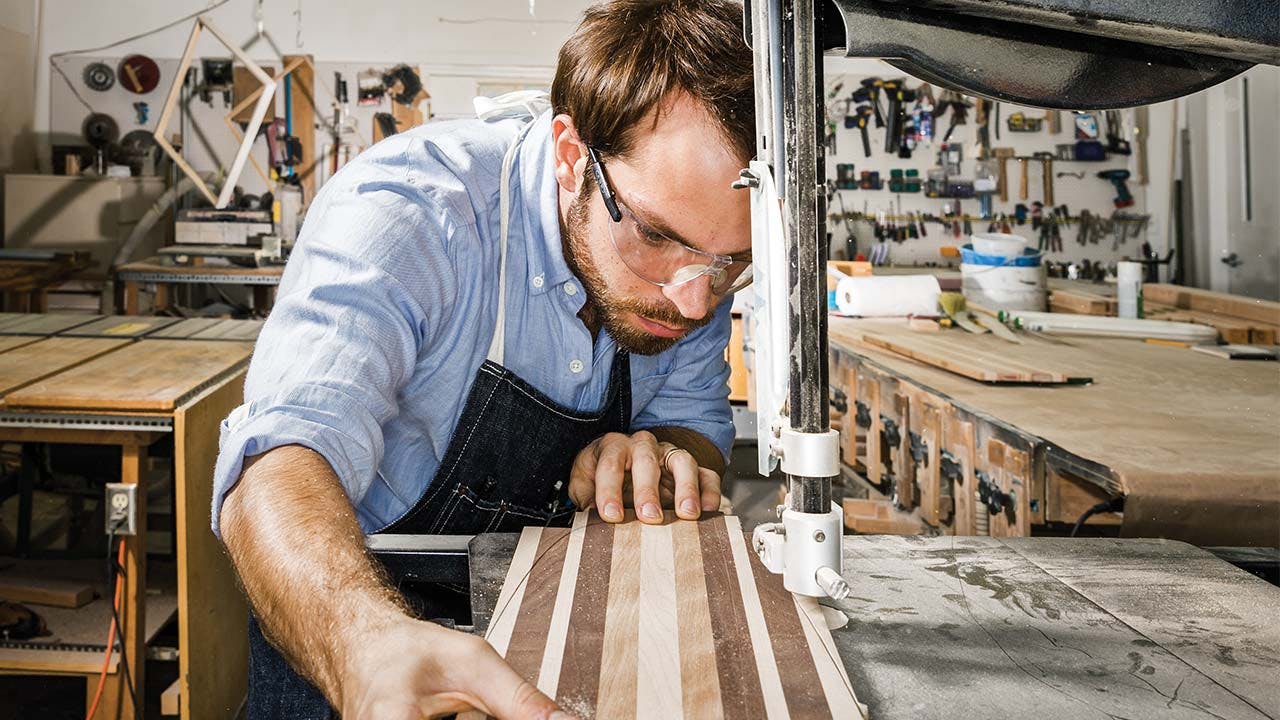 Eshelman using a band saw to cut a slab of reclaimed hardwoods into the shape of a board.
