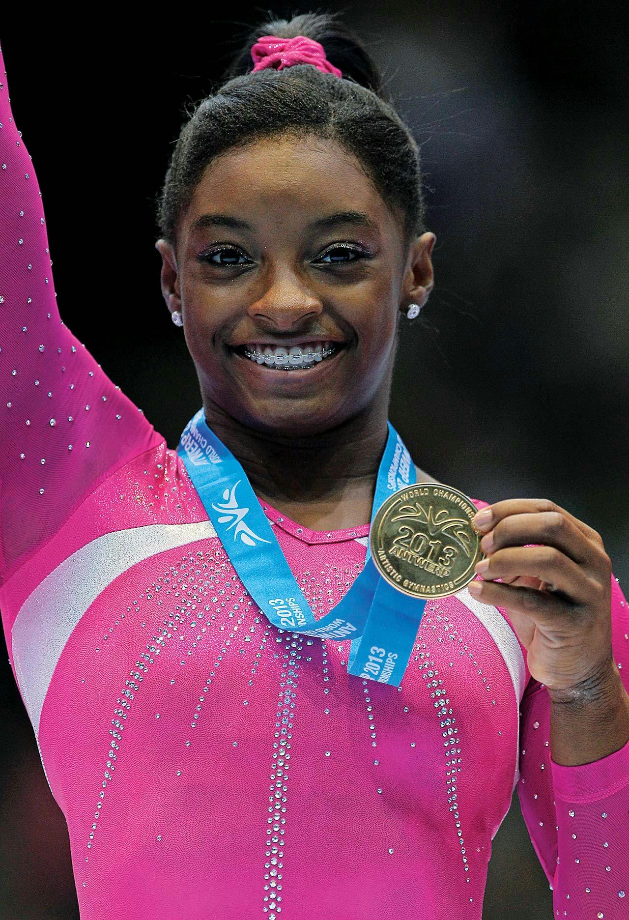 Simone Biles with her gold medal in a pink leotard. 