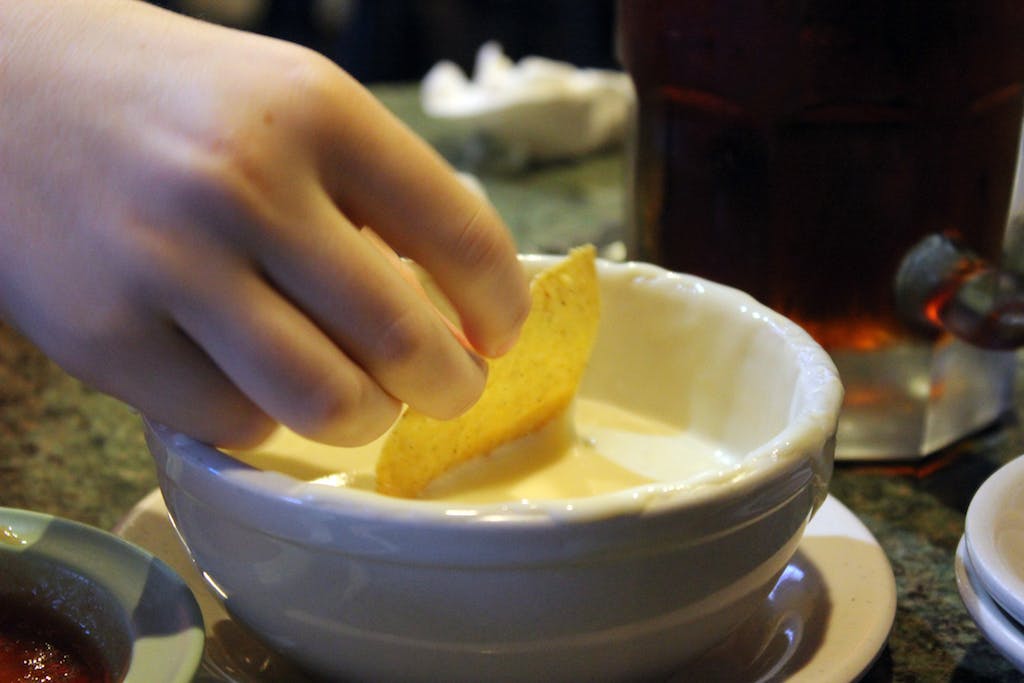 Tortilla Chip being dipped in queso. 