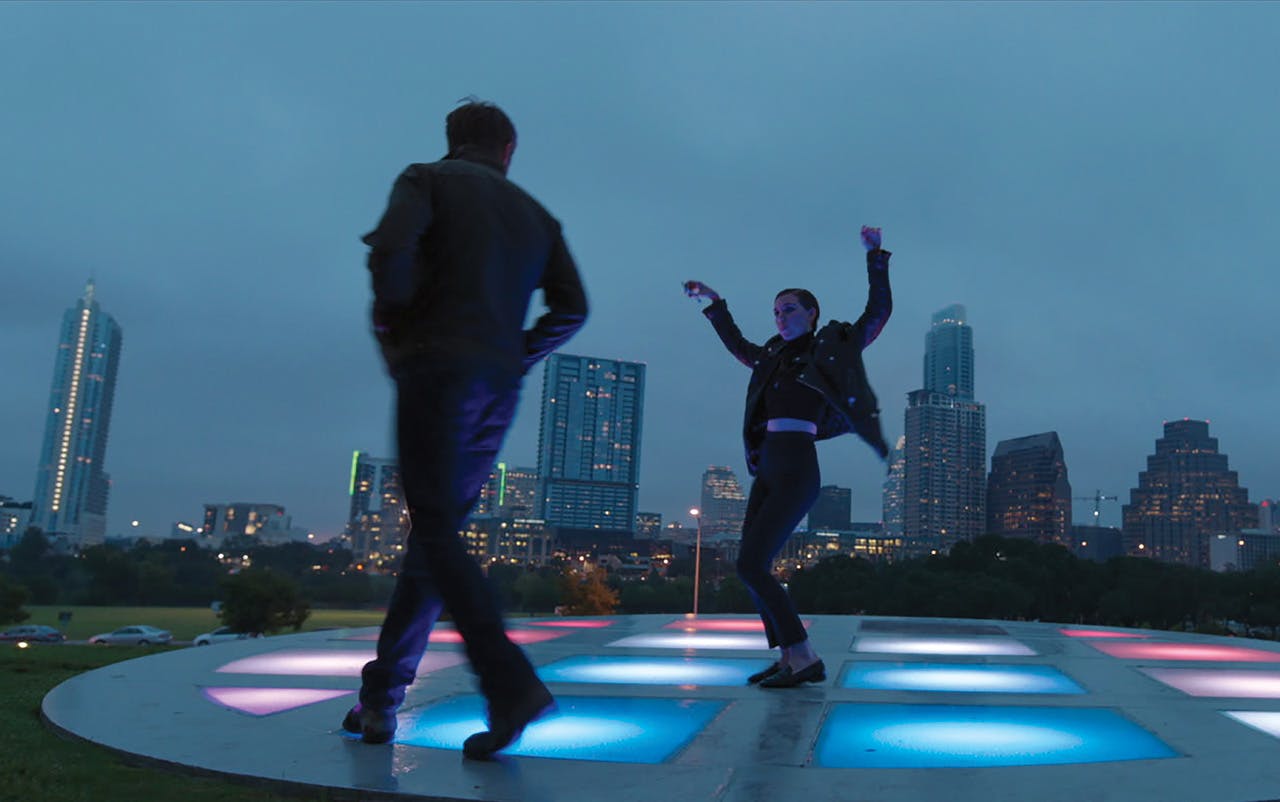 Two characters dancing on a lit-up dance floor from Song to Song. 