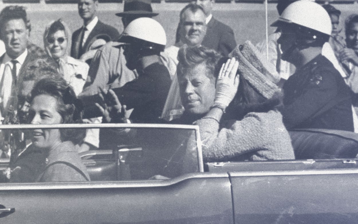 Balck and white photograph of John F. Kennedy in his car in a motorcade.