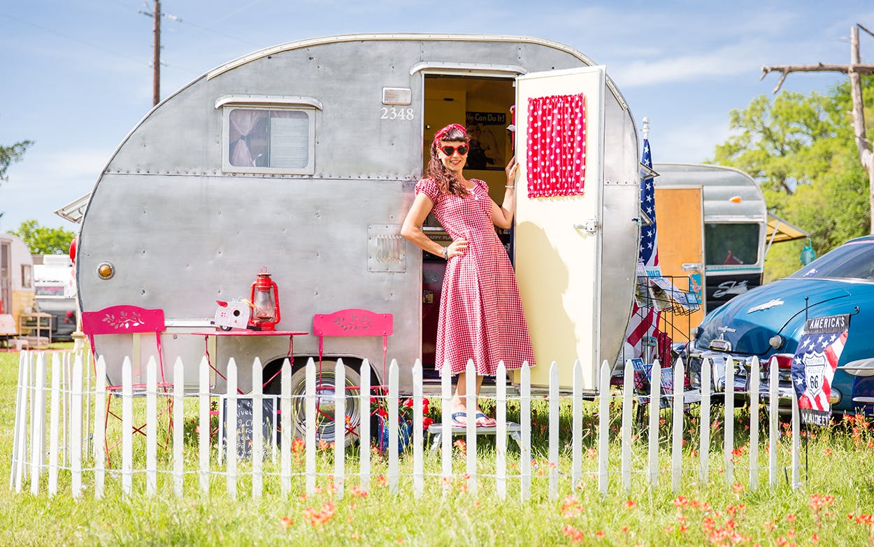 Lisa Mora in an old house dress in front of her trailer with pink accents.