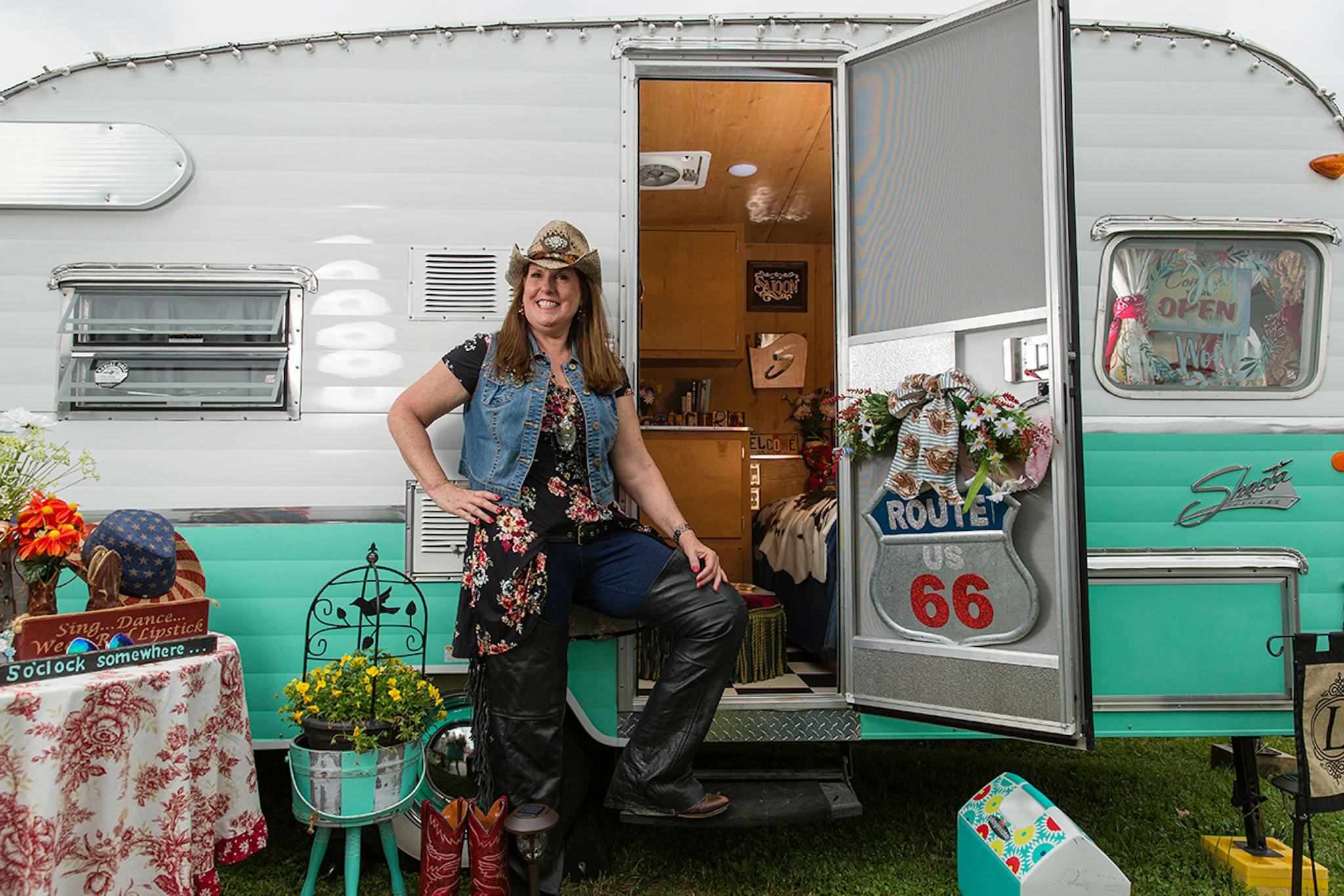 Deborah Loomis standing at t eh entrance of her white and turquoise vintage trailer.
