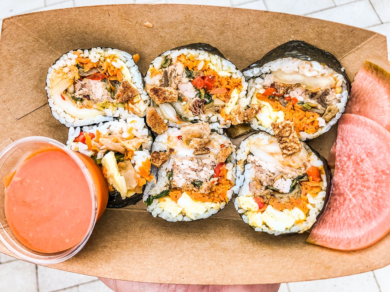 A kimbap roll, which includes scrambled egg, pulled whole hog, pickles, and rice inside a nori wrapper.