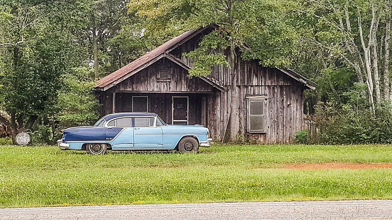 Old wooden house and old blue car. 