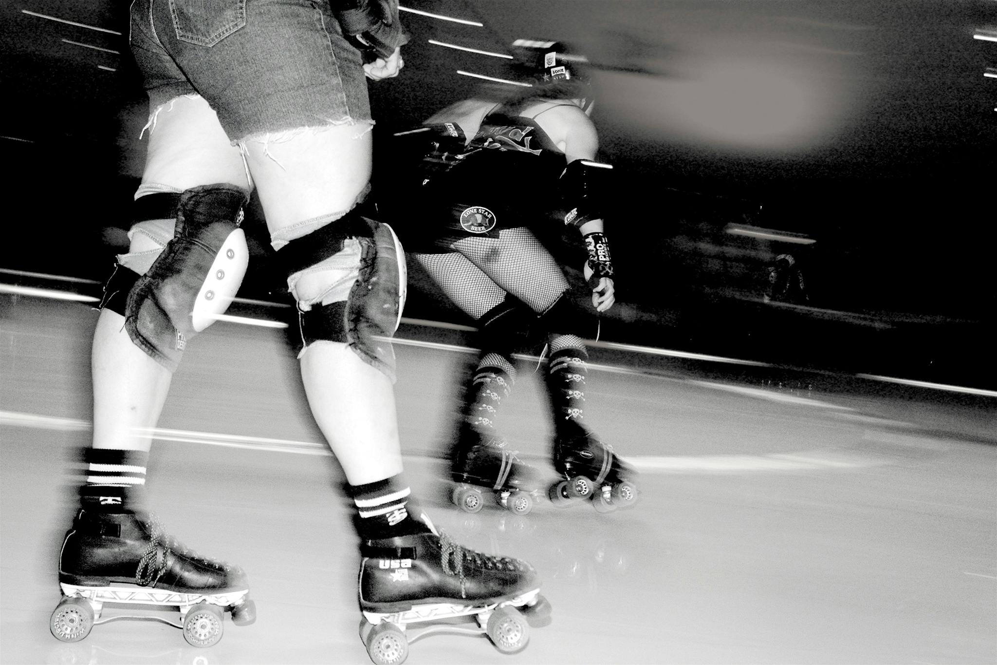 Skaters with Texas Rollergirls round the rink in a roller derby bout.