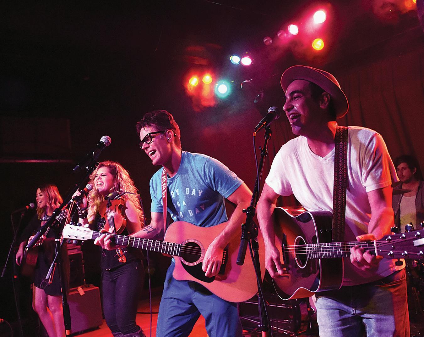 Bobby Bones playing guitar and singing on stage amongst three other musicians. 