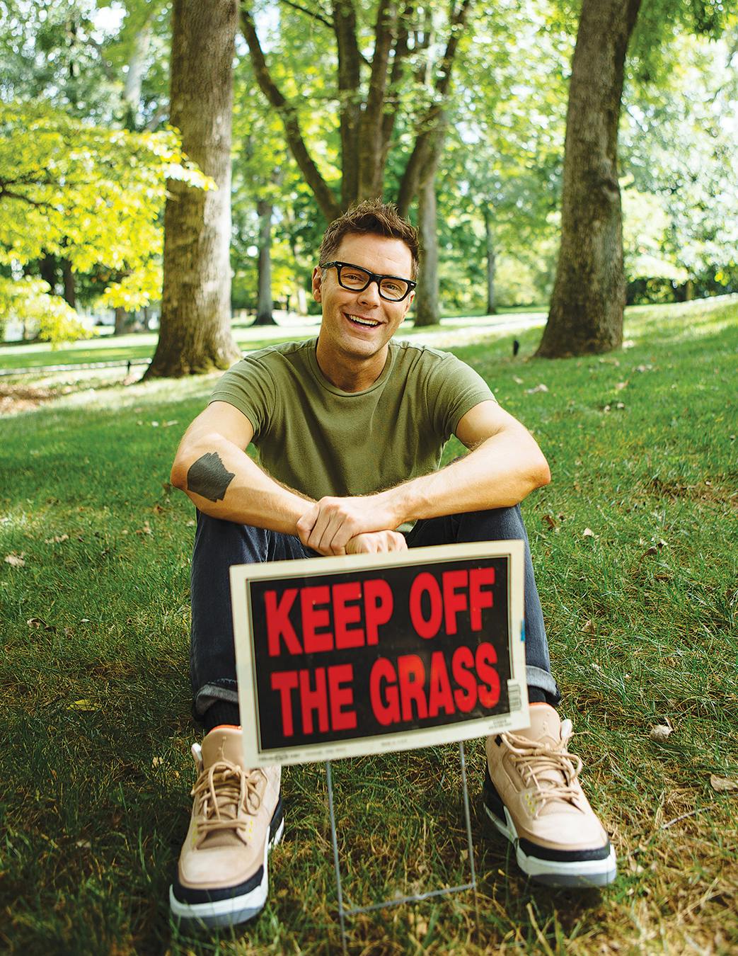 Bobby Bones sitting on his lawn behind a "keep off the grass" sign. 