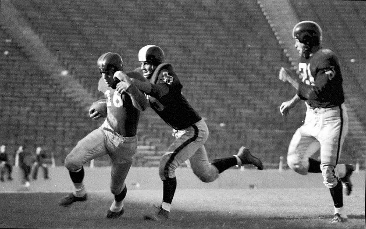 Dallas Texans players tackling Frank Gifford during the first game of the season, with empty seats in the background.