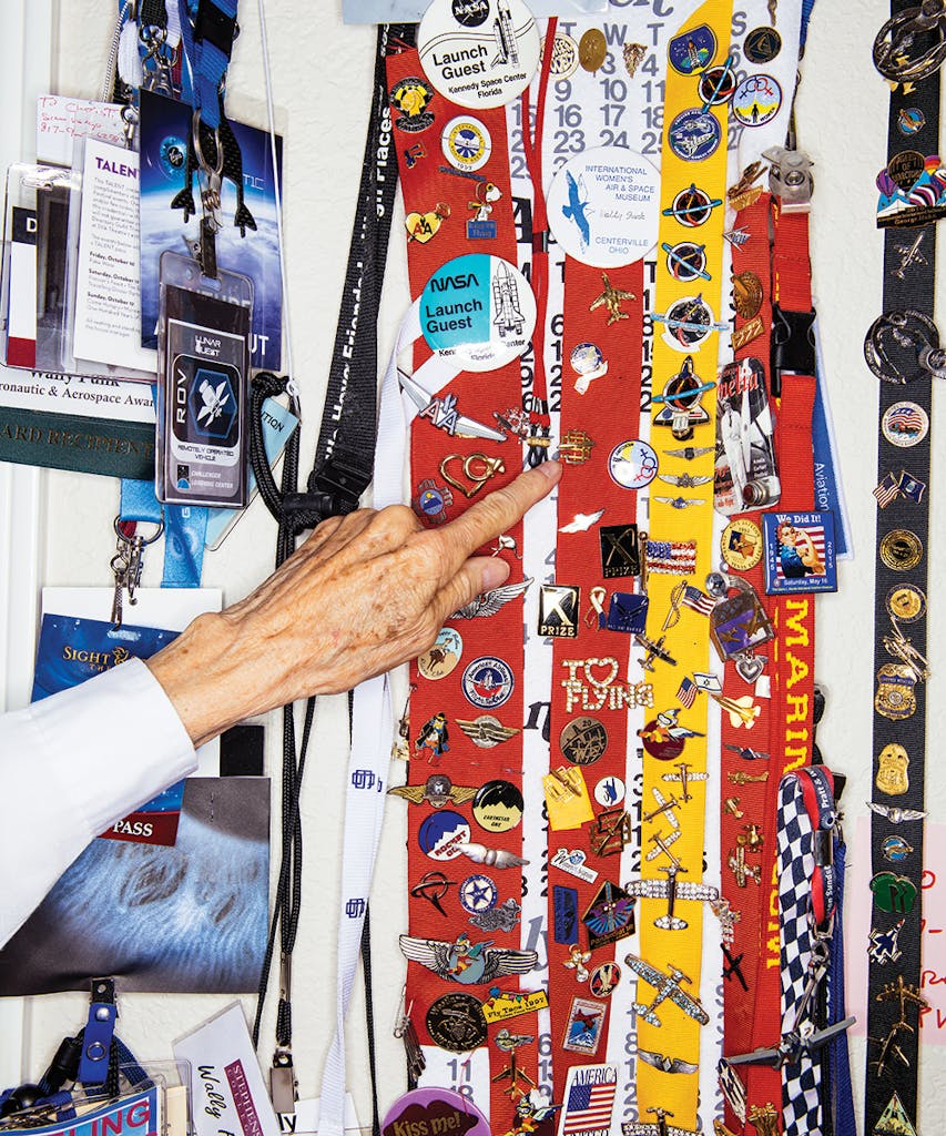 Wally Funk's hand pointing to some of her aviation and space pins hanging on ribbons. 