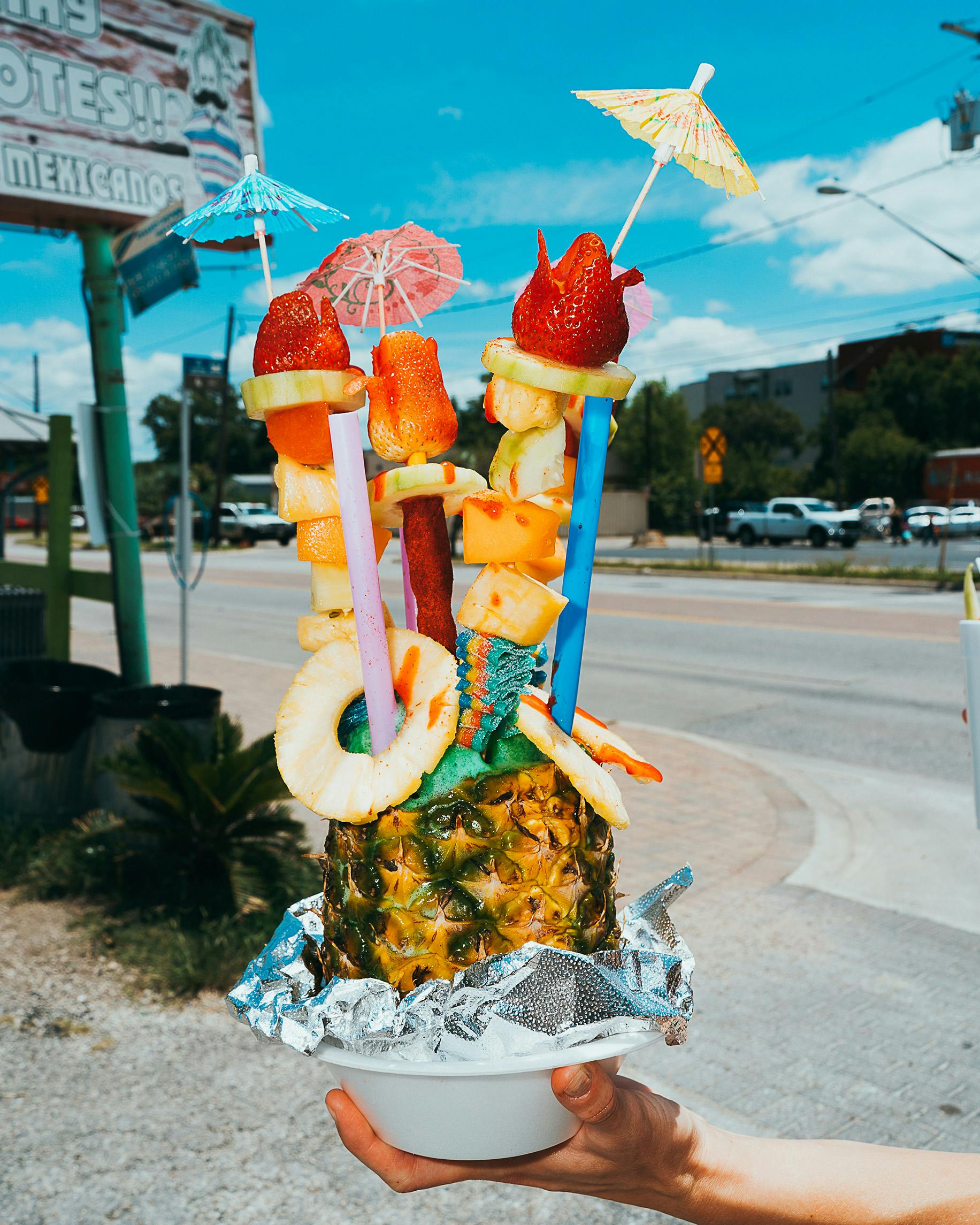 Huge raspa served in a pineapple with two straws, fruit, candy, and umbrella garnishes. 