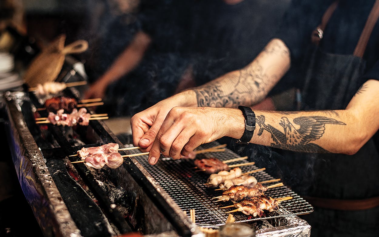 Salaryman servers cooking skewers of meat over coals