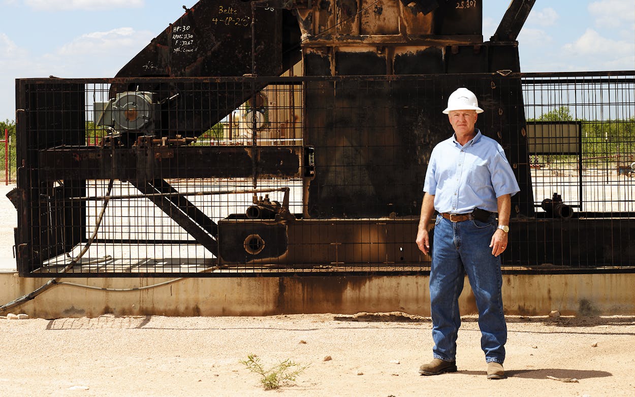 Dennis Johnson standing in front of an oil well in jeans and a hard hat.