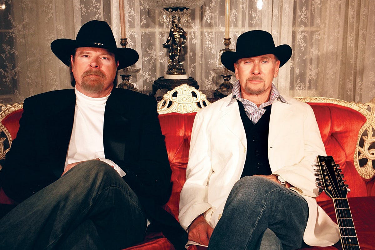 Dan and Jim on a red velvet couch, both wearing block cowboy hats. 