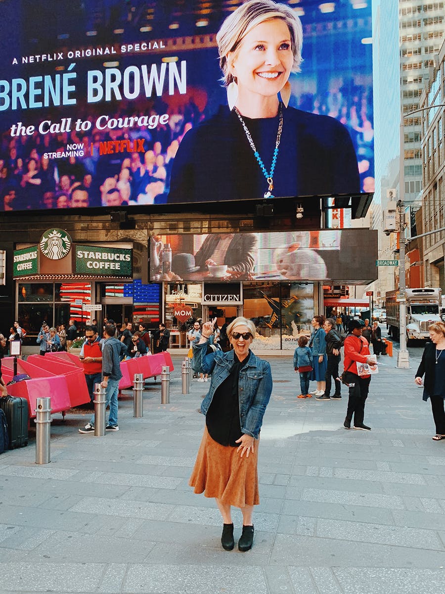 Brené Brown points up excitedly towards a large ad of herself in Times Square