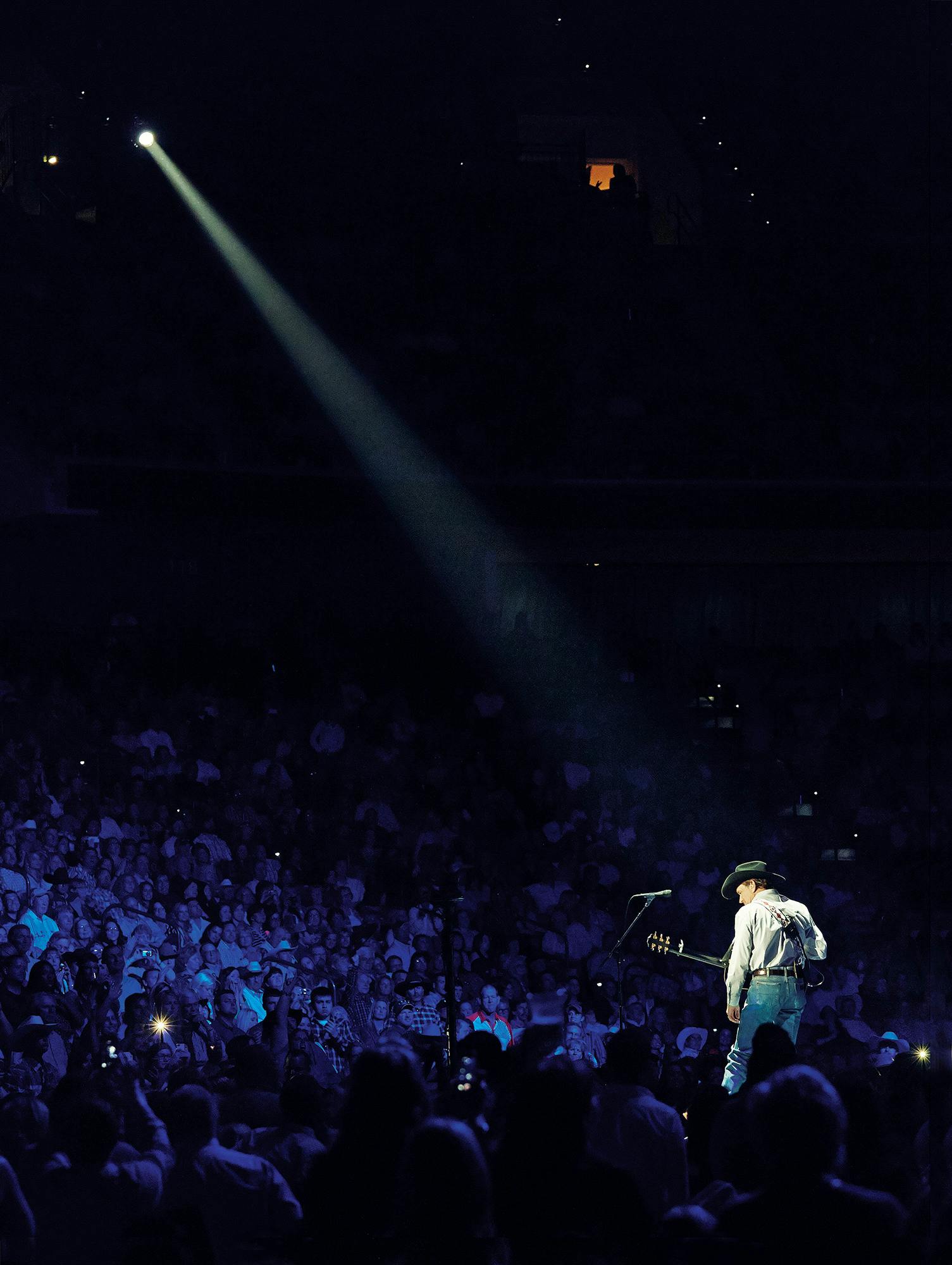 George Strait stands in the spotlight in front of concert crowd. 