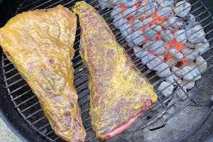 Two tri-tips smothered in a yellow run on a charcoal grill. 