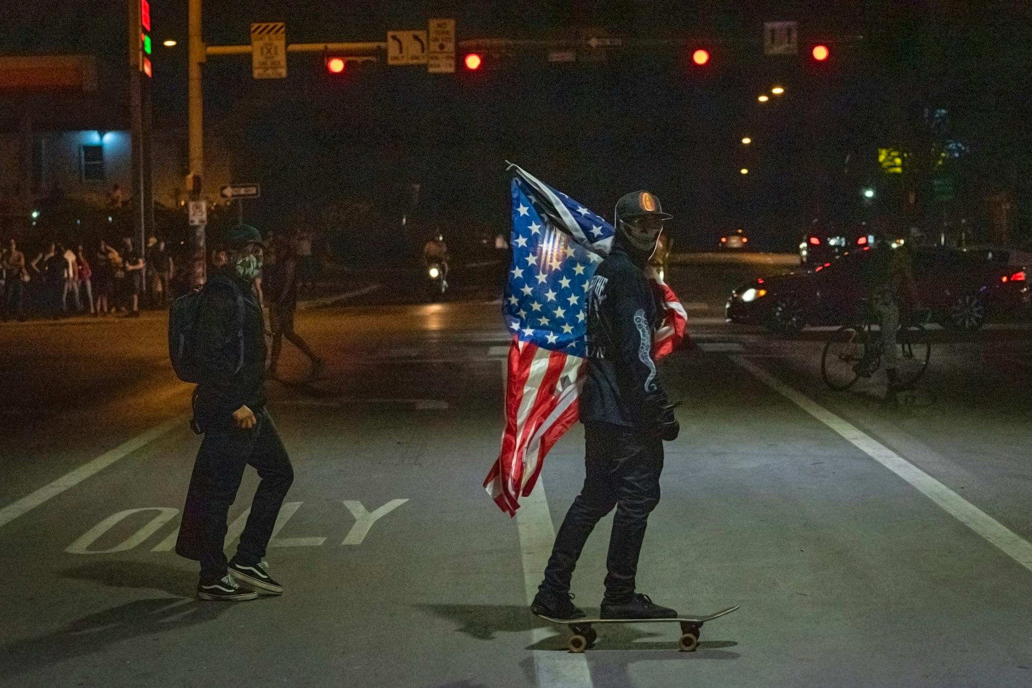A protester rides a skateboard with an American flag under I-35 at 7th Street in front of police headquarters in Austin on May 30, 2020.