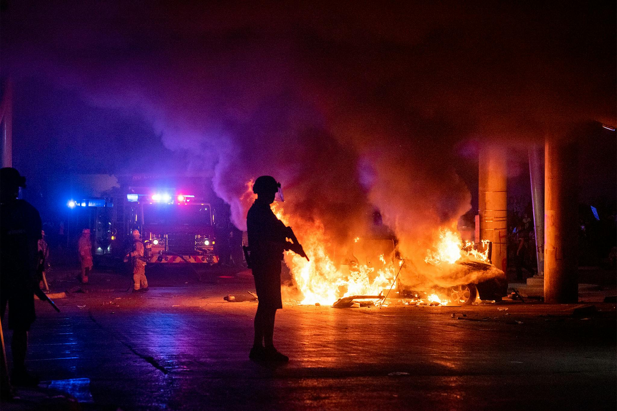 Officer protects the perimeter of a burning car under I-35 so firefighters can put it out during protests in Austin on May 30, 2020.