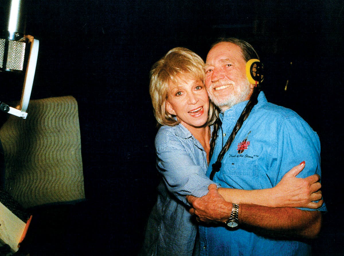 Jeannie Seely and Willie Nelson hugging and smiling at the camera in a recording booth. 