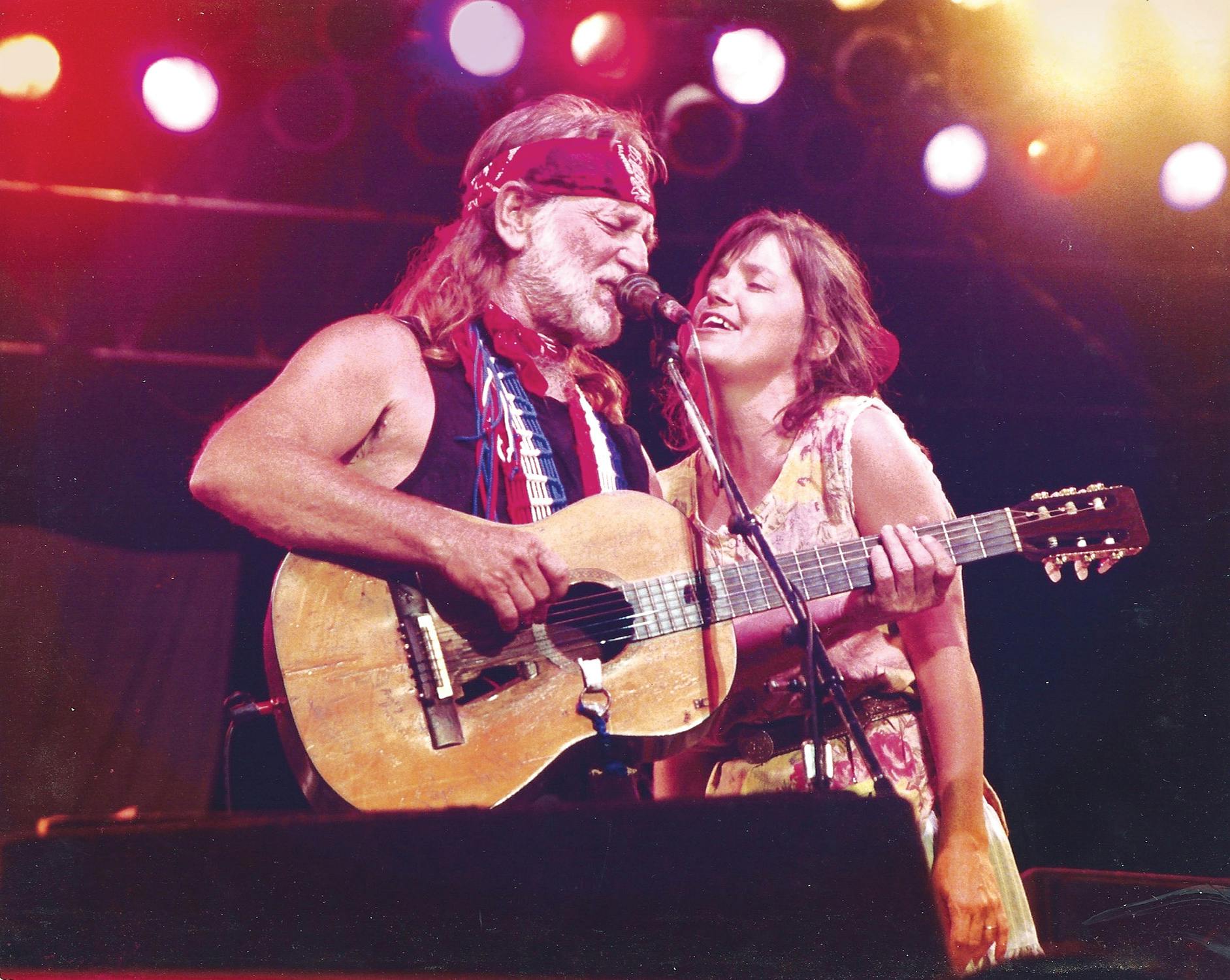 Willie and Kimmie roads winging together into a microphone against a backdrop of stage lights. 
