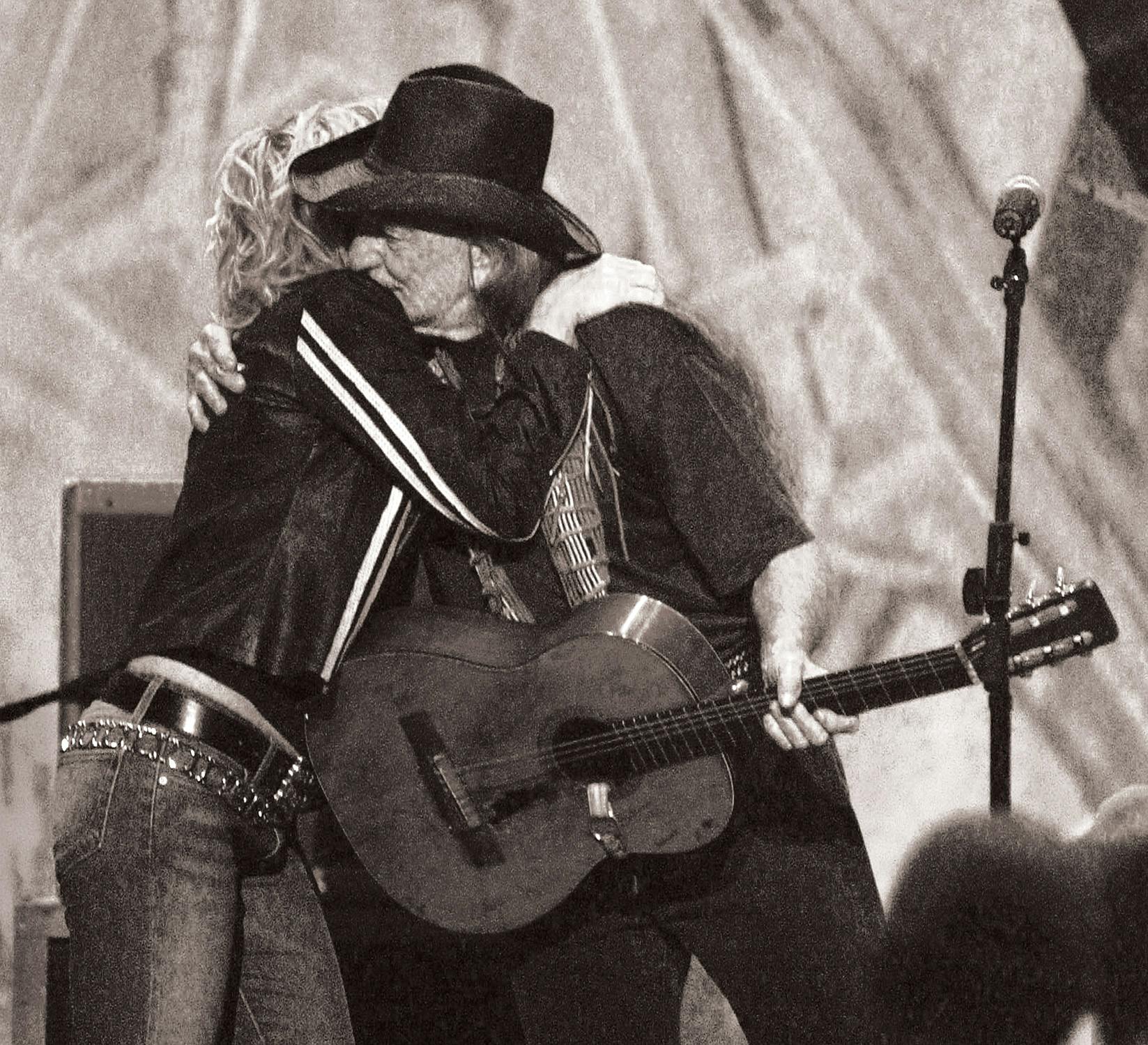 Lucinda William hugging Willie Nelson on stage. 