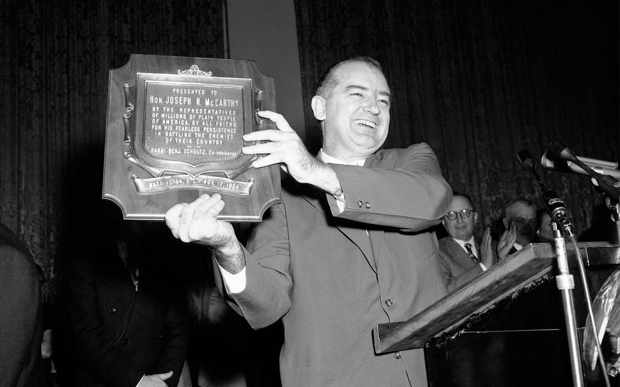 Sen. Joseph McCarthy holds aloft a plaque, misdated, which was presented to him for his “fearless persistence” in battling the enemies of America.