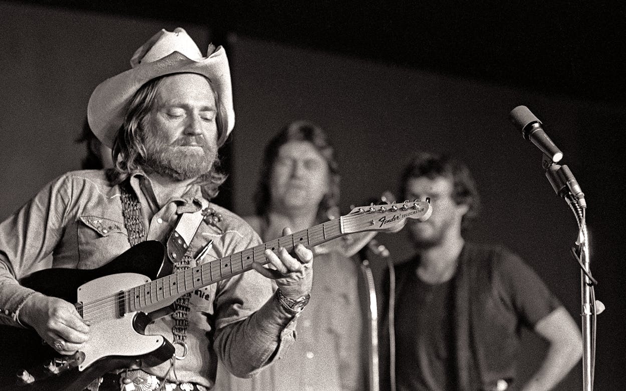 Willie Nelson playing guitar on stage.