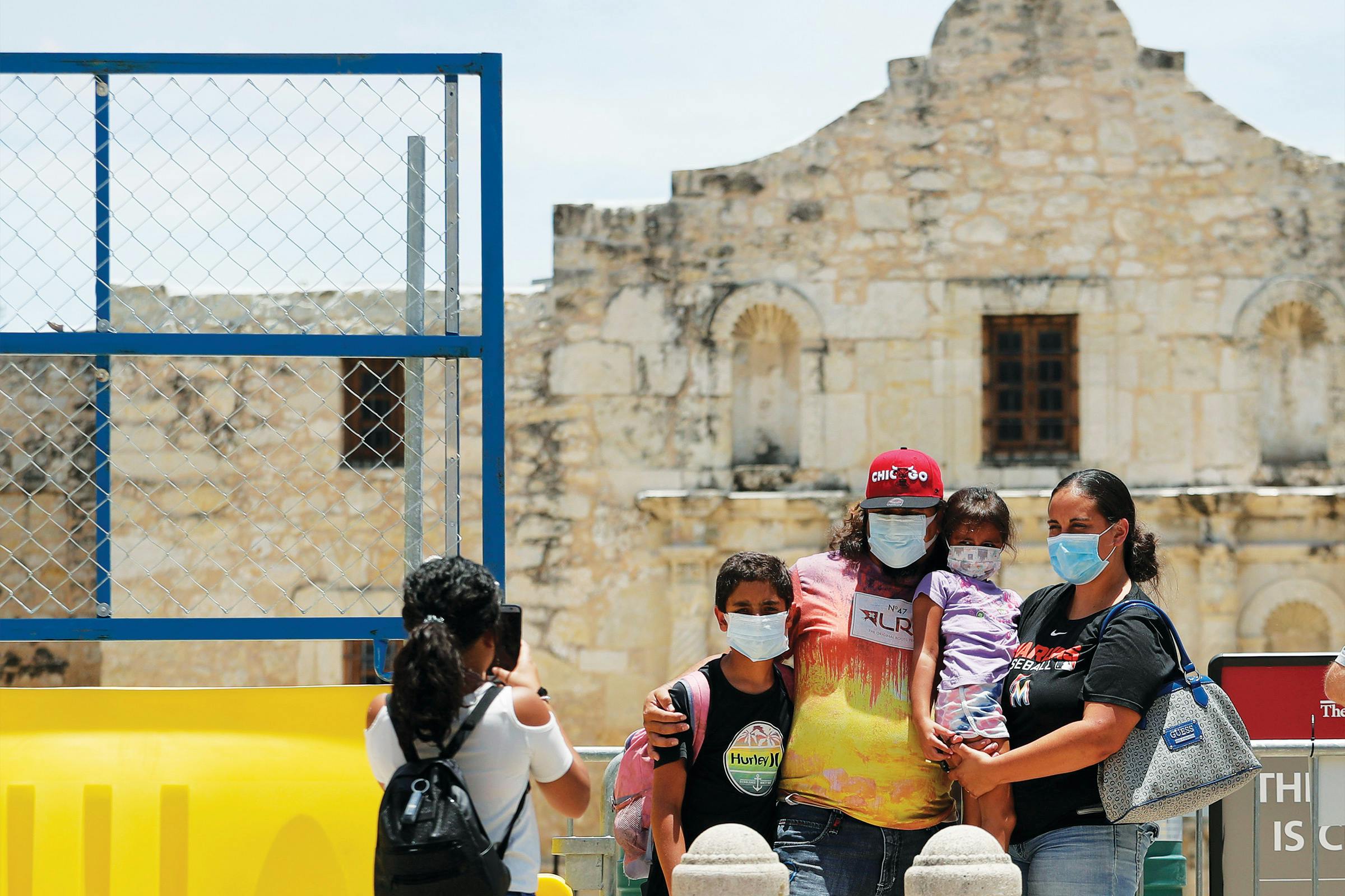 A family wearing masks taking a photo in front of the Alamo. 