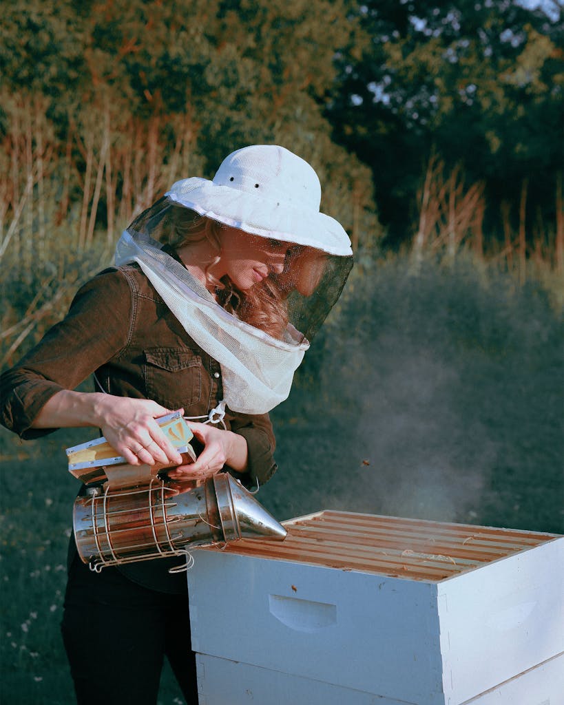 Erika Thompson in her bee veil and helmet at her hive holding a smoker.