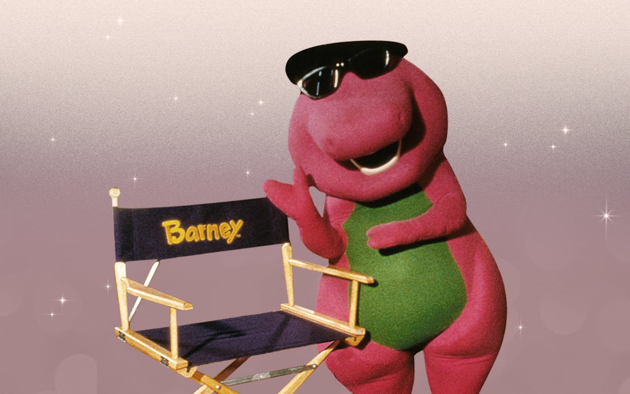 Barney the dinosaur in sunglasses next to an actor's chair.
