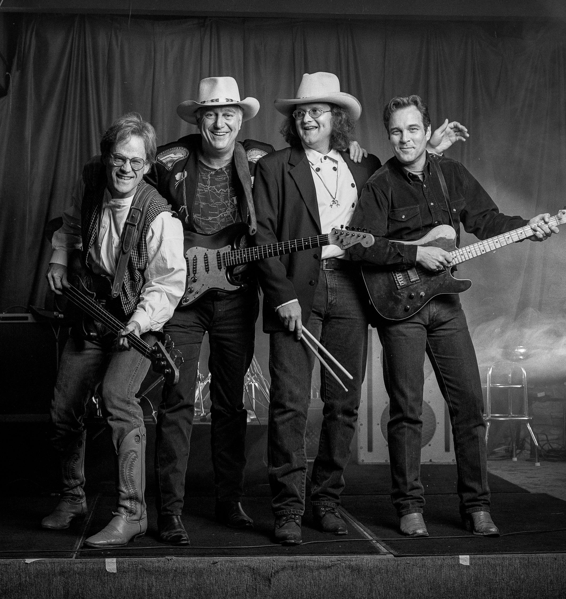 Bob Livingston, Jerry Jeff Walker, Freddie Krc, and John Inmon holding their instruments with their arms around each other.  