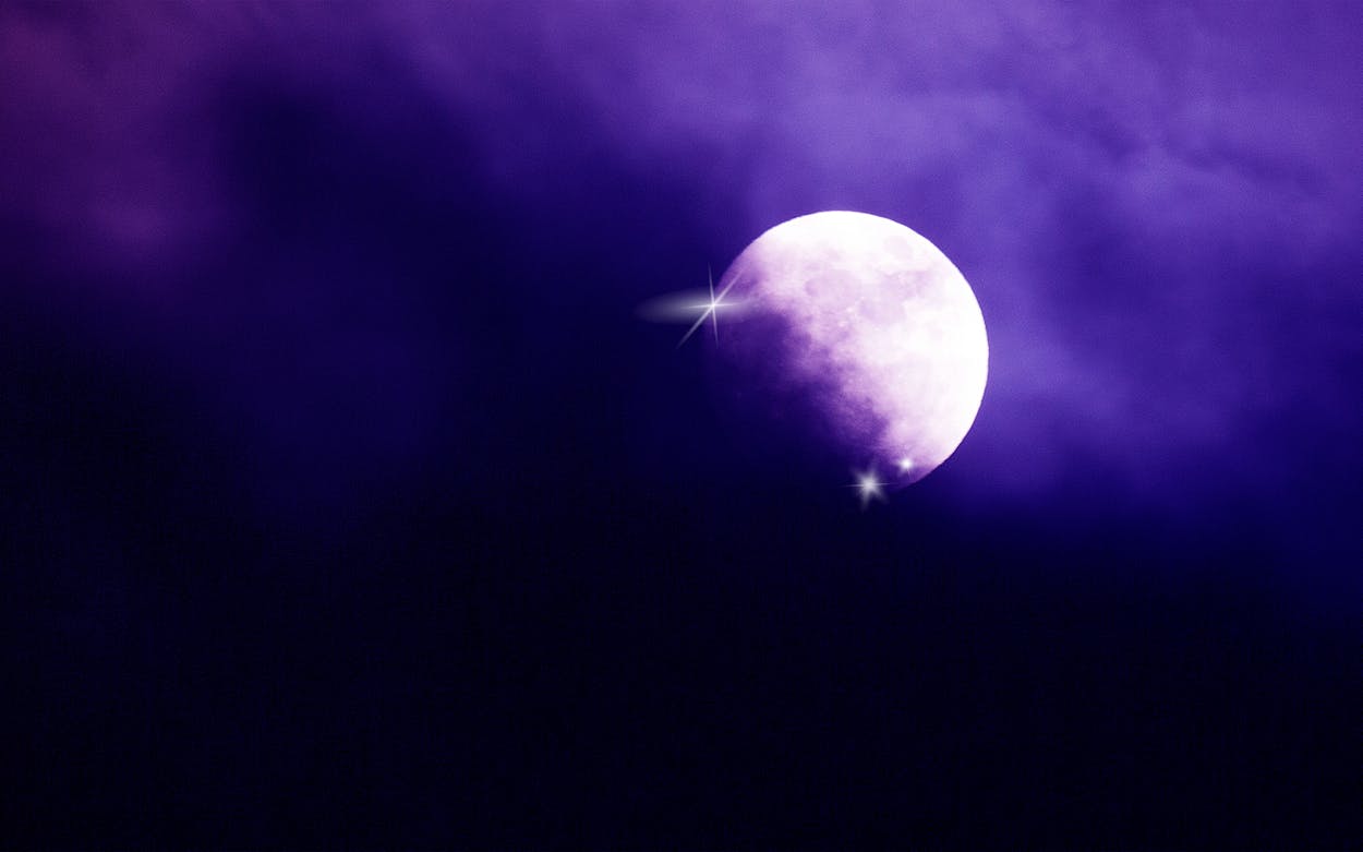 The moon glowing in a cloudy, purple sky.