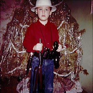 Wayne White as a child, holding his new exploring gear in front of a Christmas tree. 