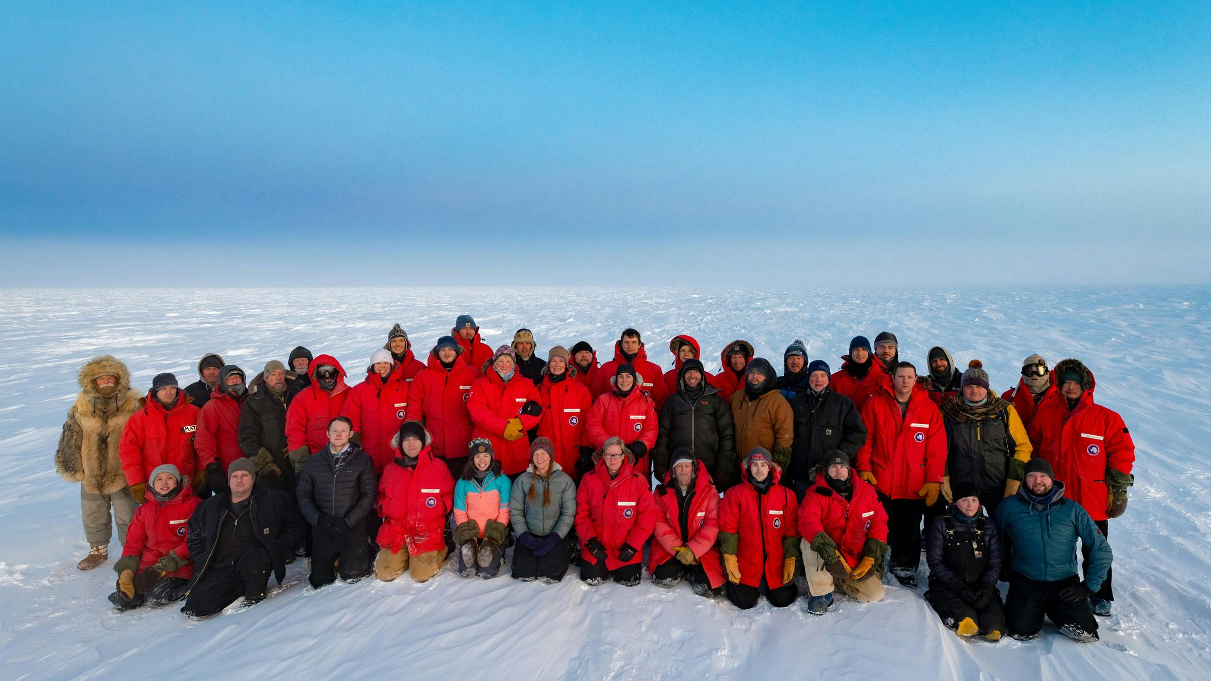 Wayne White in his wolf fur parka alongside the rest of the South Pole 2020 winter crew, wearing mostly red, insulated parkas. 